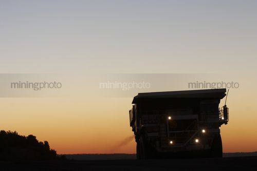 Silhouette photo of a haul truck coming over a hill in an open cut mine.  dusk and sunset behind. great generic shot. - Mining Photo Stock Library