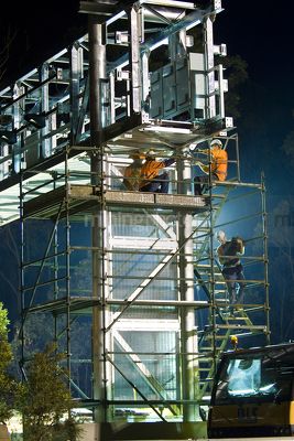 Infrastructure workers in full PPE including harness working off scaffolding at a bridge gantry site.  photo taken at night. - Mining Photo Stock Library