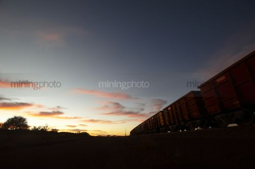 Iron ore train moving through the Pilbarra at dawn. generic photo of heavy rail. - Mining Photo Stock Library