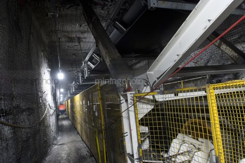 Underground conveyor belt and ducting work.  mine site worker walking in background gives scale. - Mining Photo Stock Library