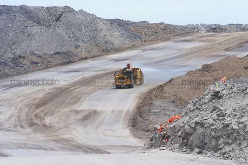 Earth scraper driving down haul access road in open cut mine site. - Mining Photo Stock Library