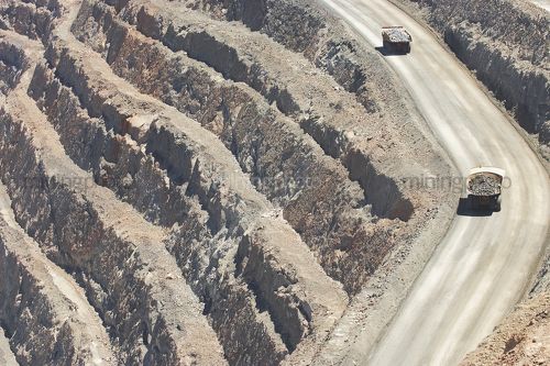 Haul trucks on access ramp in a large open cut mine.  benching below. - Mining Photo Stock Library