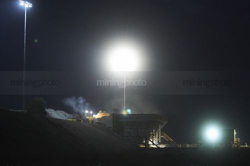 Loader loading coal into a hopper for conveyor at night - Mining Photo Stock Library