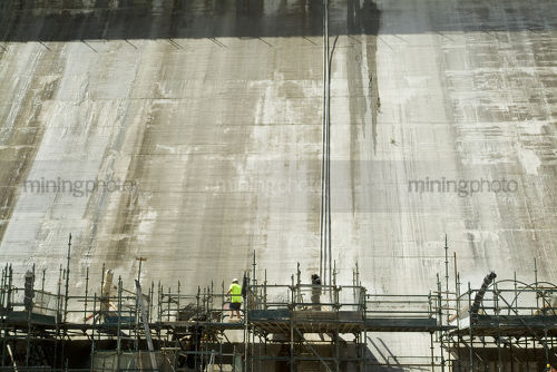 Construction worker in PPE standing atop scaffolding with DAM wall in background. - Mining Photo Stock Library