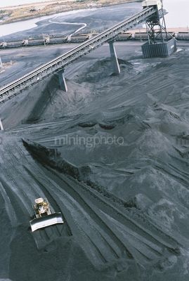 Bulldozer stockpiling coal at shipping port with loader and heavy rail behind aerial vertical image - Mining Photo Stock Library