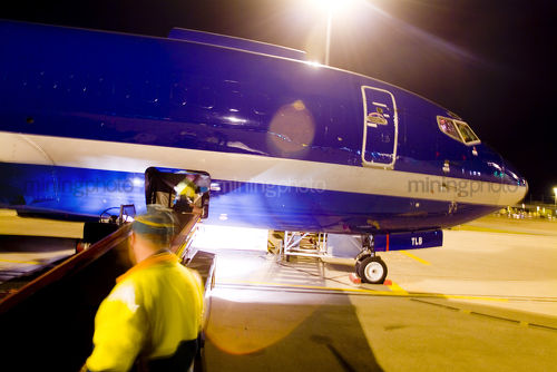 Airport worker loading cargo onto plane at night.  shot from behind. - Mining Photo Stock Library