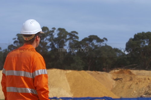 Male worker in full PPE looking out over site.  room on right hand side for copy. - Mining Photo Stock Library
