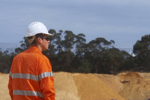 Male worker in full PPE looking out over site.  room on right hand side for copy. - Mining Photo Stock Library