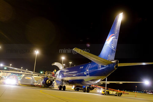 Larger cargo plane being loaded at night at airport.  workers faintly seen checking hold. - Mining Photo Stock Library