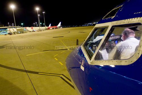 Pilot in plane checking procedures at airport at nigth.  shot from outside plane looking in and from over pilots back. - Mining Photo Stock Library