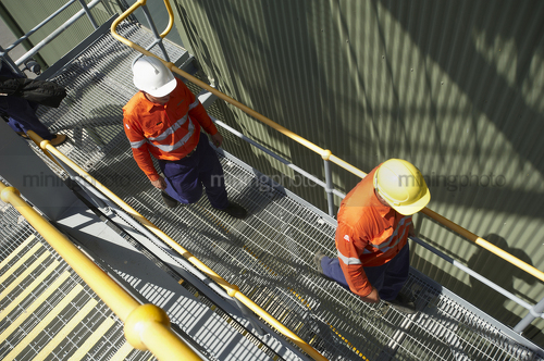 Photo of two mine site workers in full PPE walking up stairs.  faces cannot be seen. - Mining Photo Stock Library
