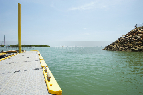 Looking over edge of a marine jetty with boats and mangroves on the horizon line. - Mining Photo Stock Library