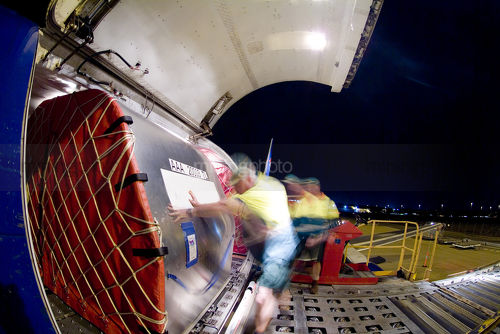 Workers in PPE rolling large cargo boxes into hold of plane. shot at night. - Mining Photo Stock Library