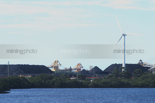 Great photo of a large wind generator and in the background is a reclaimer loading stockpiles of coal.  large dam in foreground. - Mining Photo Stock Library