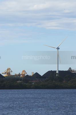 Great photo of a large wind generator and in the background is a reclaimer loading stockpiles of coal.  large dam in foreground. - Mining Photo Stock Library
