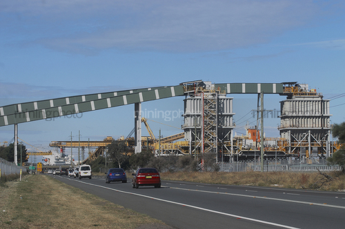 Coal conveyor travelling over cars on main road. Shiploader in background. - Mining Photo Stock Library
