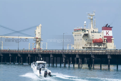 Recreation boat amongst ore terminal and large ship - Mining Photo Stock Library