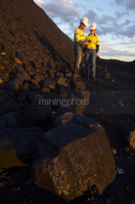 Close up photo of coal with mine workers male and female in full PPE in background out of focus.  shot at dusk with great afternoon light.  vertical photo. - Mining Photo Stock Library