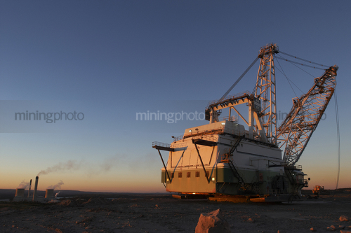 Dragline at open cut coal mine in afternoon light with coal fired power station stacks in background. - Mining Photo Stock Library