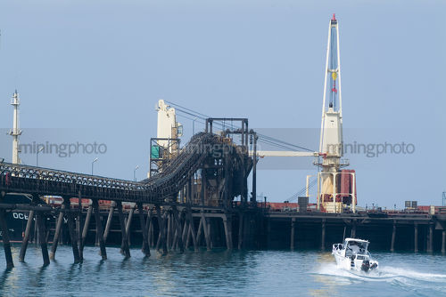 Recreation boat cruising around iron ore being loaded onto ship at terminal - Mining Photo Stock Library