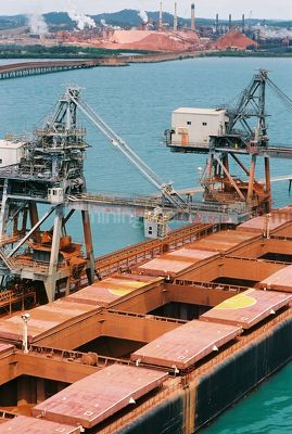 Ship loader conveyor loading bauxite into ships holds with processing plant in background. aerial shot. - Mining Photo Stock Library