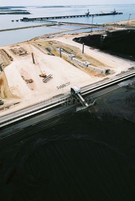 Aerial shot of coal stockpile with port construction and shiploading terminal in background - Mining Photo Stock Library