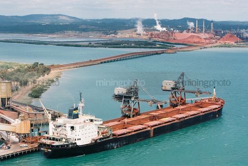 Ship being unloaded at wharf with alumina processing plant in background - Mining Photo Stock Library