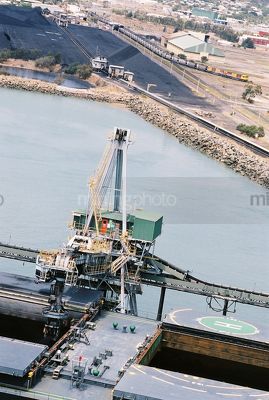 Closeup of ship being loaded with  coal at wharf with heavy rail train moving through background. - Mining Photo Stock Library