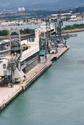 Heavy ship wharf awaiting ship to load with marina and processing plants in the background - Mining Photo Stock Library