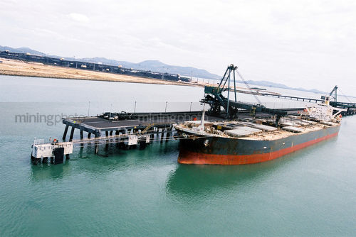 Ship loaders loading coal by conveyor into hold of ship. aerial image shot from sea looking to land. - Mining Photo Stock Library