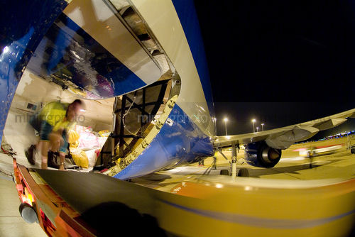 Airport worker inside plane loading freight from conveyor at night. - Mining Photo Stock Library