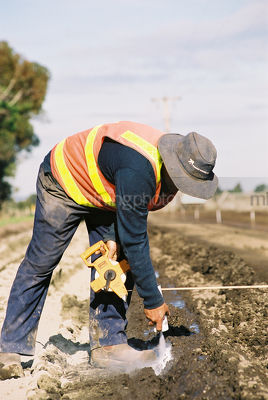 Surveyor in full ppe with tape measure marking out road during construction - Mining Photo Stock Library