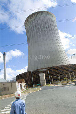 Worker walking onsite past cooling tower of power station - Mining Photo Stock Library