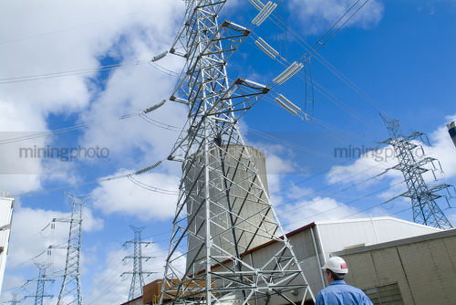Worker looking up at transformer tower and cooling tower at power station on bright blue sky day - Mining Photo Stock Library