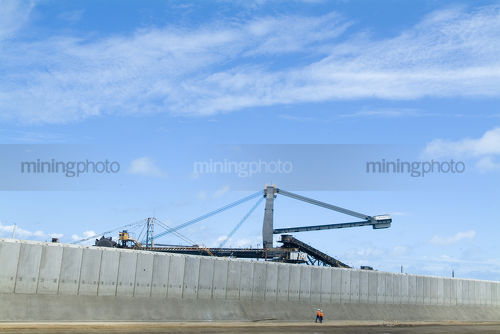 Workers walking in huge concrete bulk coal storage pits at ship terminal with reclaimers in the background - Mining Photo Stock Library