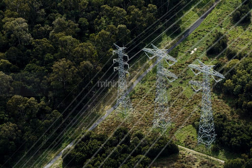 Aerial looking down at 3 parallel transformer electricity towers in forest - Mining Photo Stock Library