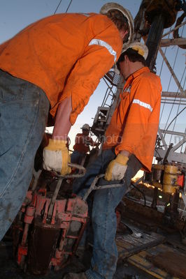 Workers working together to lay pipe on a drill rig - Mining Photo Stock Library
