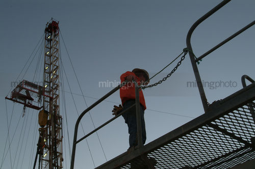 Worker on walkway with drill rig derrick behind - Mining Photo Stock Library
