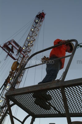 Silhouette of a worker on walkway with drill rig derrick behind - Mining Photo Stock Library