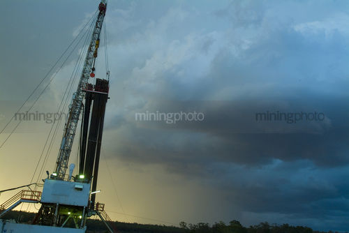 Drill rig and derrick shot at sunset with storm behind - Mining Photo Stock Library