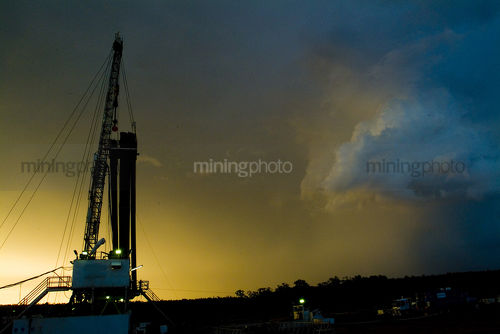 Land based drill rig shot at sunset with storm passing by behind - Mining Photo Stock Library