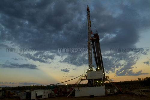 Sunset and storm behind drill rig  - Mining Photo Stock Library