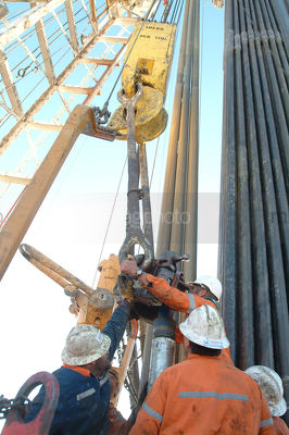 Workers attaching equipment to the derrick on a drill rig - Mining Photo Stock Library