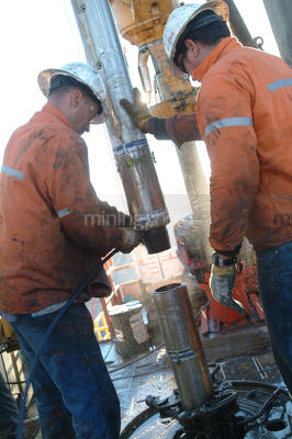 Drill rig workers attaching pipe casing to hole - Mining Photo Stock Library