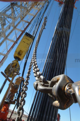 Chain and cables on oil and gas rig with derrick behind. - Mining Photo Stock Library