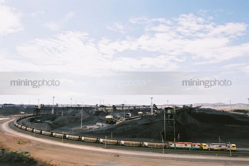 Aerial shot of coal train at wharf terminal with stockpiled coal in background - Mining Photo Stock Library