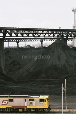 Aerial shot of coal train at wharf terminal with stockpiled coal in background - Mining Photo Stock Library