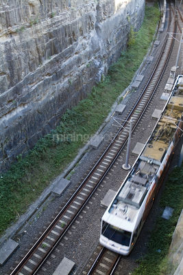 Light rail train coming from a tunnel  next to steep high rock walls.  shot from above - Mining Photo Stock Library