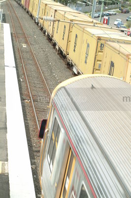 Looking down on a goods freight train passing a light rail passenger train next to a domestic station - Mining Photo Stock Library