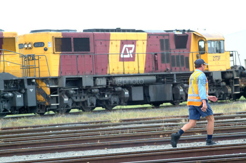 Rail worker crossing tracks with heavy train engine in background. - Mining Photo Stock Library